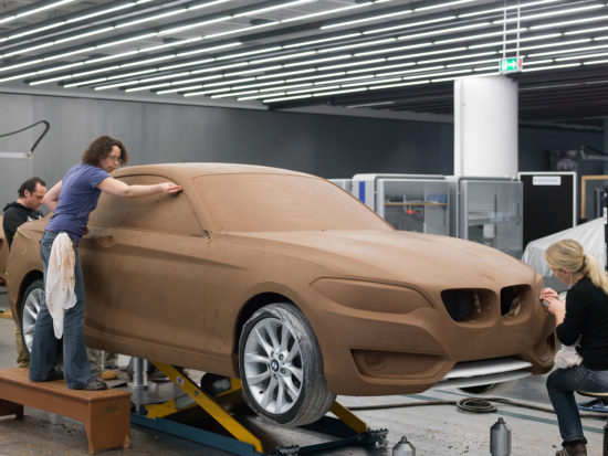 Designers shaping a full-size clay model of a car by hand in a studio. CYPHR scored it 5% likely AI.